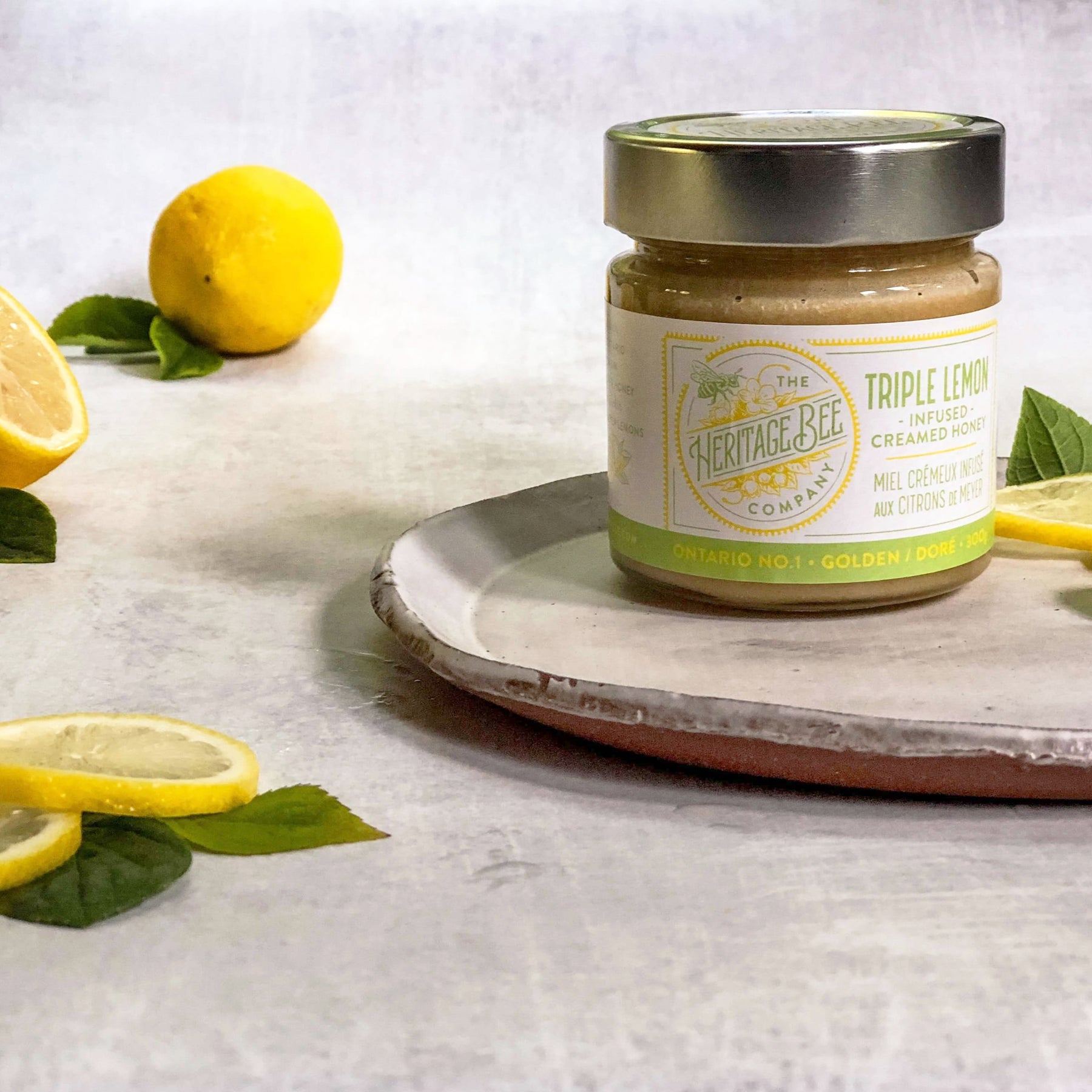 A jar of Heritage Bee Co's triple lemon infused creamed honey pictured alongside Meyer lemons. 